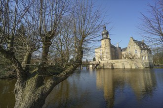 A moated castle surrounded by bare trees and a moat under a blue spring sky, Borken, North