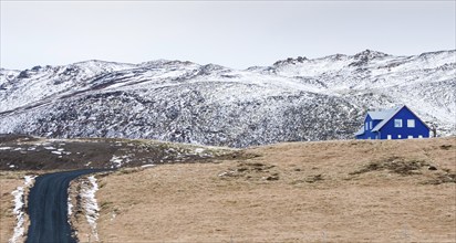 Icelandic landscape with blue chalet farm house in Reykjanes peninsula, Mountains covered in snow