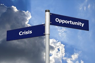 Street sign in front of dark clouds symbolizing contrast between 'crisis' and 'opportunity'