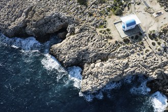 Drone aerial photograph of Cape Greco peninsula with Agioi Anargyroi christian church on the rocks.