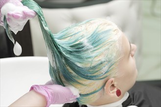 Washing green hair color of young woman with shampoo in sink. Working hairdresser in pink