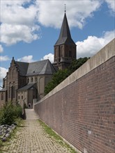 Historic church with high tower next to a long brick wall under a blue sky, Emmeriich, Rhine, North