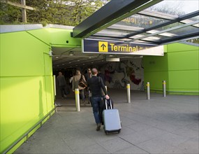 Passengers with luggage walking into tunnel terminal, London Stansted airport, Essex, England, UK