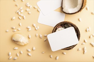 White paper business card with coconut and seashells on orange pastel background. Top view, flat