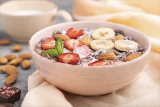 Chocolate cornflakes with milk, strawberry and almonds in ceramic bowl on gray concrete background