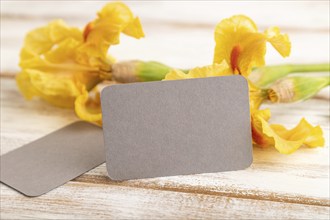 Gray business card with iris yellow flowers on white wooden background. side view, copy space,