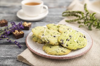 Green cookies with chocolate and mint on ceramic plate with cup of green tea and linen textile on