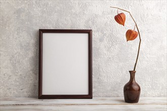 Brown wooden frame mockup with physalis in ceramic vase on gray concrete background. Blank,