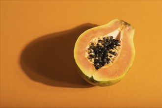 Ripe cut papaya on orange pastel background. Side view, close up, hard light. Tropical, healthy