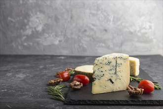 Blue cheese and various types of cheese with rosemary and tomatoes on black slate board on a black