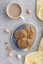 Homemade oatmeal cookies with a cup of cocoa and a yellow textile on a gray concrete background.