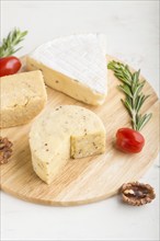 Cheddar and various types of cheese with rosemary and tomatoes on wooden board on a white wooden