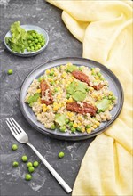 Quinoa porridge with green pea, corn and dried tomatoes on ceramic plate on a gray concrete