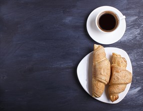 Two croissants with cup of coffee on white plate on black wooden background. top view with