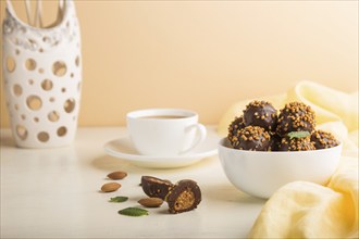 Chocolate caramel ball candies with almonds and a cup of coffee on a white and orange background