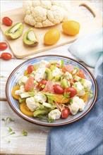 Vegetarian salad of cauliflower cabbage, kiwi, tomatoes, microgreen sprouts on white wooden