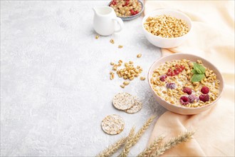 Wheat flakes porridge with milk, raspberry and currant in ceramic bowl on gray concrete background