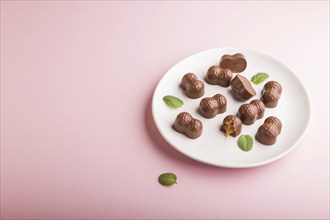 Chocolate caramel candies on a pastel pink background. Side view, copy space, close up