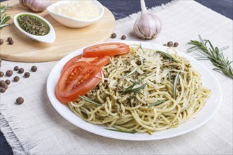 Spaghetti pasta with pesto sauce, tomatoes and cheese on a linen tablecloth on black wooden