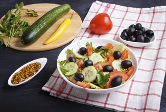 Vegetarian salad of tomatoes, cucumbers, parsley, olives and mustard on linen tablecloth and black