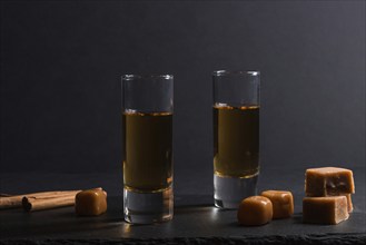 Glass of whiskey with caramel candies on a black stone slate board on black background. Side view,