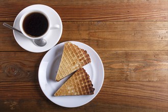 Waffle sandwiches with boiled condensed milk in plate on brown wooden table with cup of coffee.