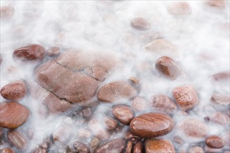 Close-up of water and round, bright red stones on a seashore on the north-west coast of Scotland