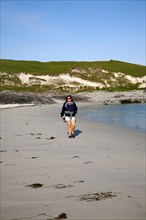 Woman walking on sandy beach at Bagh a Deas, South Bay, Vatersay island, Barra, Outer Hebrides,