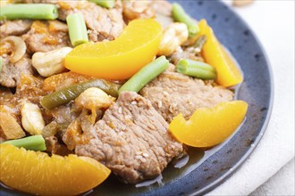 Fried pork with peaches, cashew and green beans on a black concrete background. Side view, close