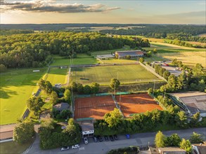 Aerial view of a sports facility with tennis courts and football pitches, surrounded by woods and