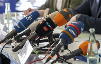 Microphones from various radio and television stations are on the table at a press conference