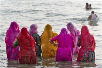 Hindu pilgrims, woman in colourful saris, take a holy dip in the sea in front of sunrise at Ghat