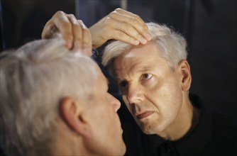 Symbolic photo on the subject of a high hairline and receding hairline. A man looks at his hairline