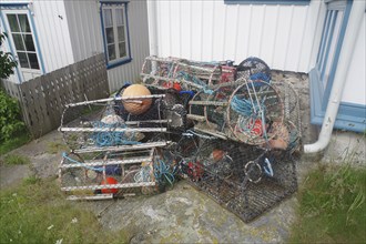 Stacked fishing baskets and ropes next to a white house, the typical equipment for the fishing