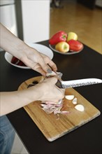 Close-up view of female hands using kitchen knife to peel garlic cloves