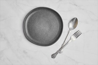 Top view of empty ceramic plate and spoon with fork on marble background