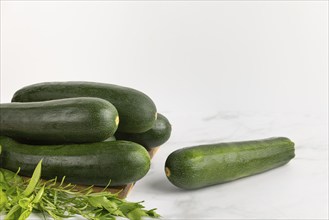 A single courgette next to a pile of courgettes and herbs on a wooden board with a light-coloured