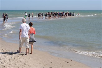 Ttourists standing at the northern tip of Denmark where the Baltic Sea and North Sea meet at Skagen