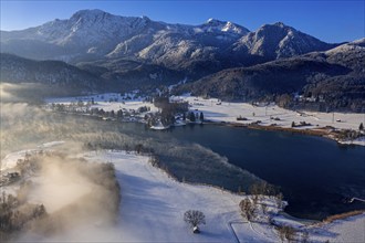 Aerial view of a lake in front of mountains in winter, snow, fog, morning light, view of