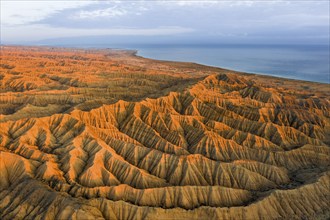 Landscape of eroded hills, badlands at sunset, Lake Issyk Kul in the background, aerial view,