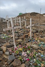 Row of graves with crosses and flowers on a stony cemetery under a grey sky, remote Arctic Inuit