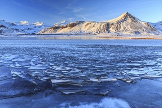 Ice floes on a lake in front of snowy mountains, sun, evening light, snow, winter, Snaefellsnes,