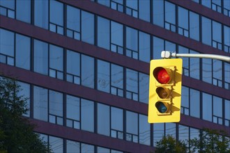 A traffic light system with the red light shining in front of a modern high-rise building with many