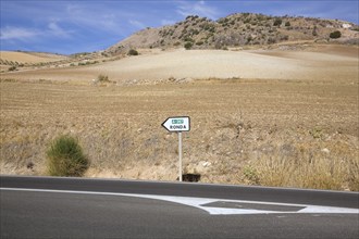 Black asphalt road and road sign in the middle of arid landscape indicating the direction to Ronda,