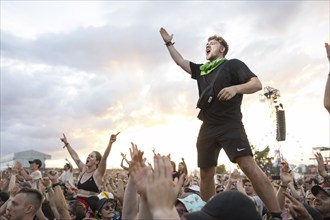 A festival visitor stands on the hands of two people during the performance of the band Feine Sahne