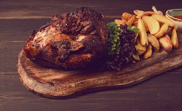 Pork knuckle, in soy-honey sauce, with fried potatoes, on a wooden chopping board, homemade, no