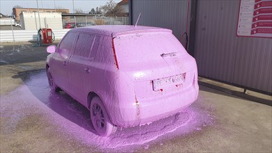 A car is covered in pink foam and is parked in a car wash, Skoda Fabia, Ilsede, Peine district,