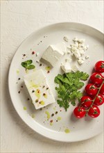 Feta cheese, for salads, with cherry, green butter, greens, on a white plate, appetizer, top view,