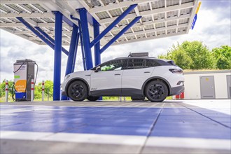 Electric vehicle being charged at a modern charging station under a solar roof, green landscape,