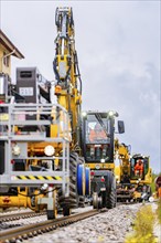 Yellow construction machinery on rails working under a slightly cloudy sky, track construction